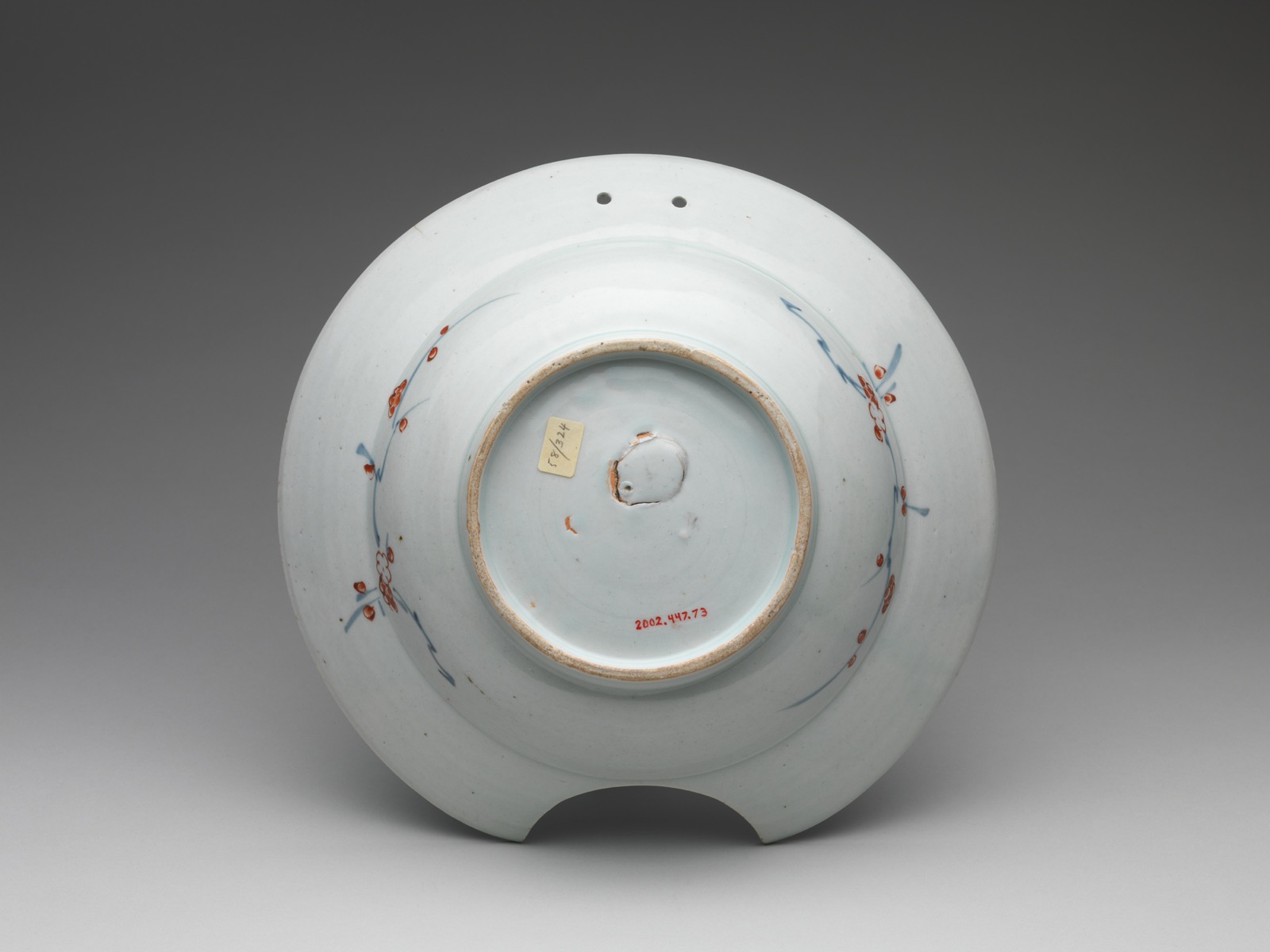 The underside of a Japanese porcelain barber's bowl of the late 17th to early 18th century, carrying a painted accession number and a small pasted inventory label